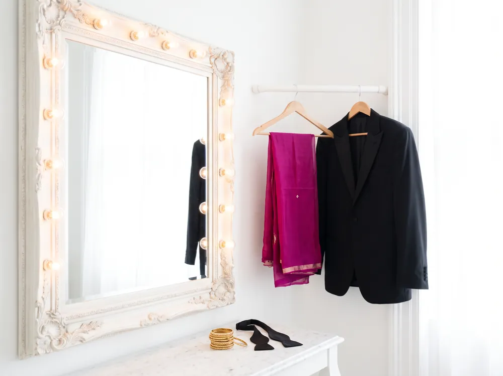 A dressing room mirror ringed with bulbs, a magenta dupatta and a black tuxedo jacket hanging side by side