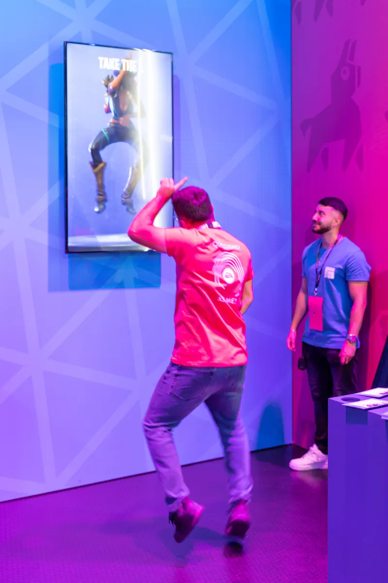 A visitor in a red shirt mimics a Fortnite dance on a screen at Gamescom