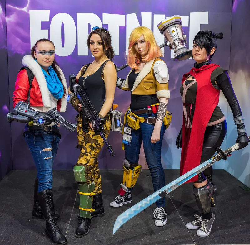 Four Fortnite cosplayers posing in front of a large Fortnite logo
