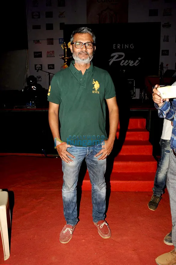 Nitesh Tiwari in glasses and a green polo shirt standing on a red carpet