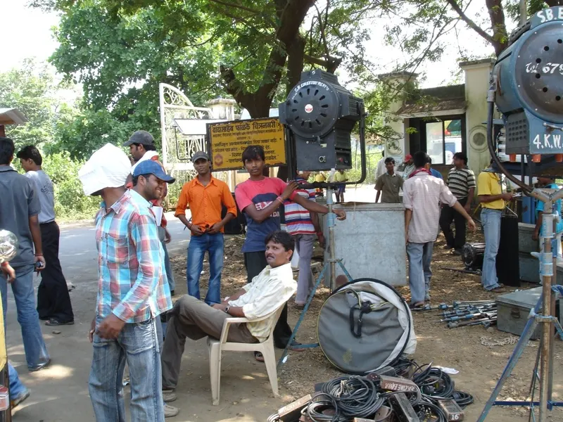 Crew members with studio lights and cables beside the Film City entrance sign in Mumbai