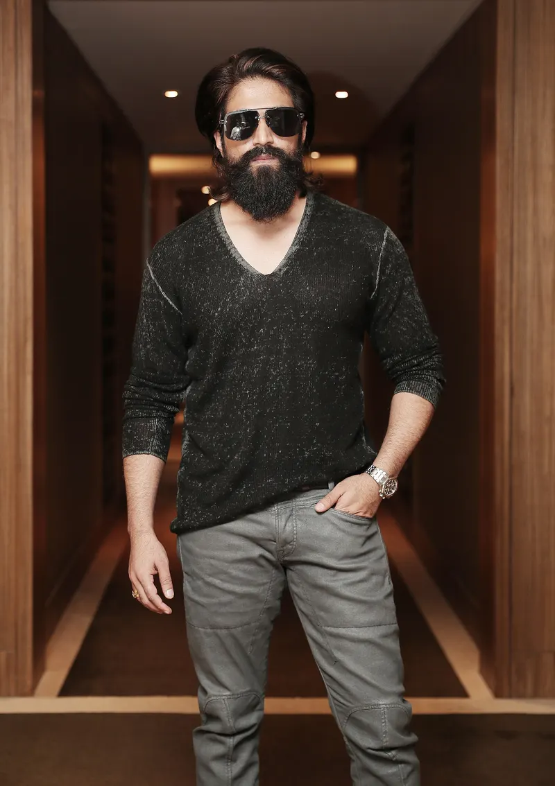 Yash with long hair, a full beard and dark sunglasses standing in a hotel corridor