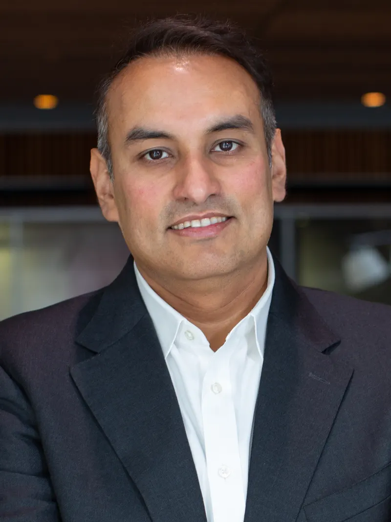 Namit Malhotra in a dark suit and open-necked white shirt, smiling