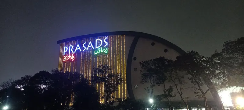 The illuminated Prasads multiplex building in Hyderabad at night behind trees