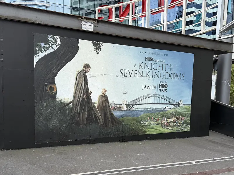 Large painted mural showing two figures under a tree beside the Sydney Harbour Bridge with the show title