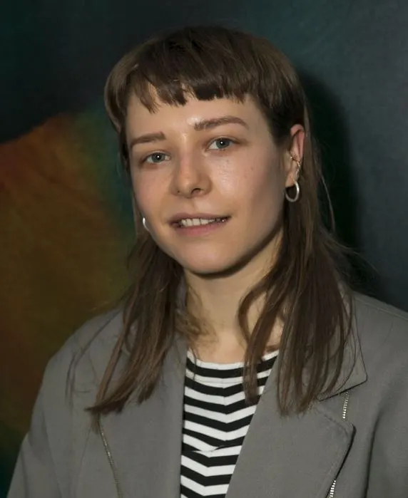 Emma D'Arcy with a fringe and striped top, smiling slightly