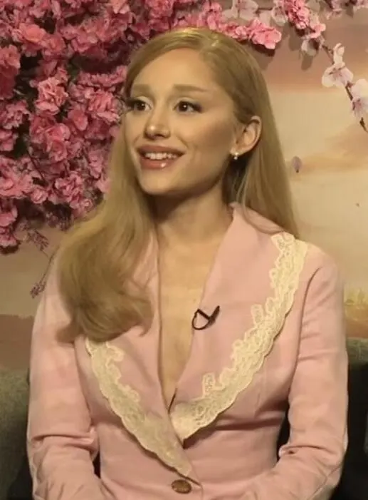 Ariana Grande smiling in a pink jacket during an interview