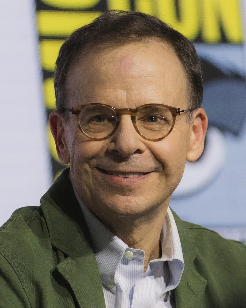 Rick Moranis in glasses and a green jacket, smiling