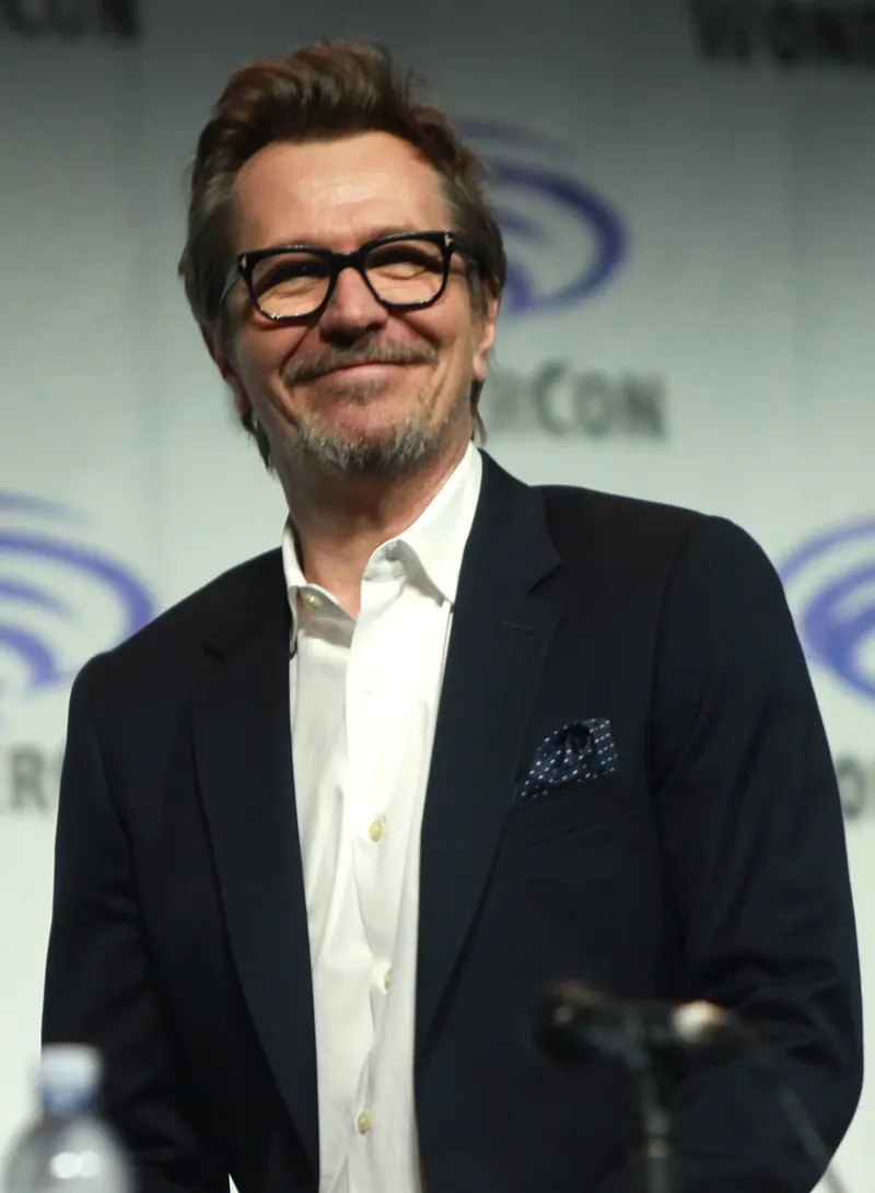 Gary Oldman in glasses and a dark suit at a panel