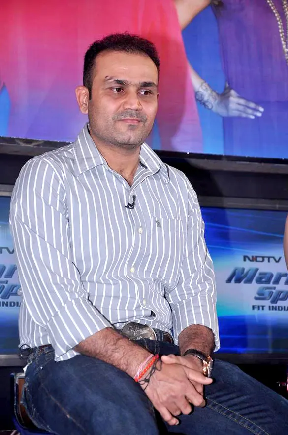Virender Sehwag seated on stage in a striped shirt