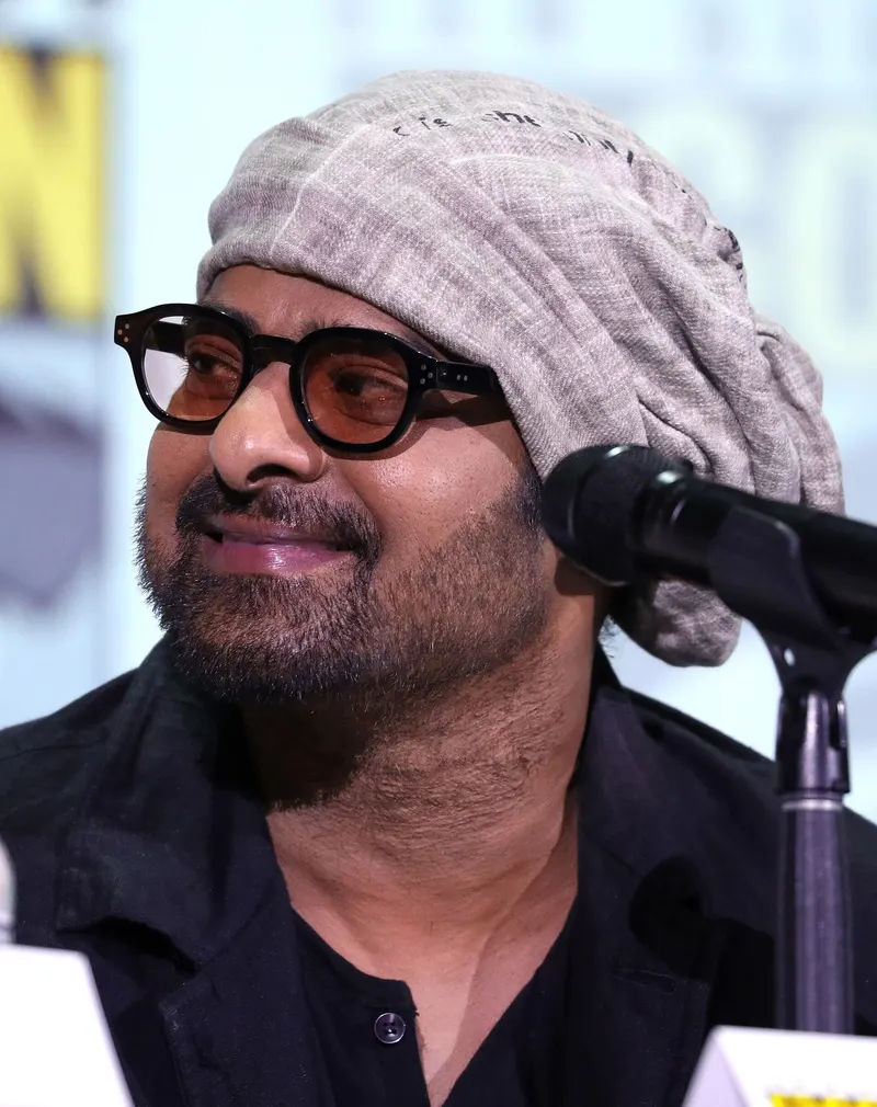 Prabhas in a knitted cap and glasses speaking into a microphone