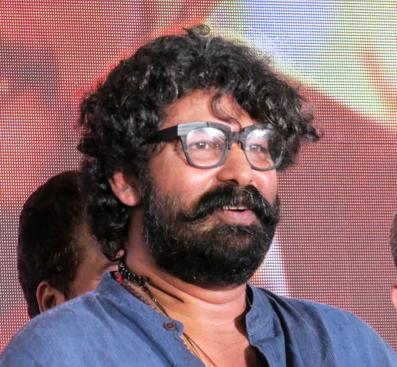 Joju George with curly hair and glasses smiling