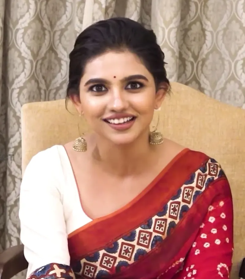 Mamitha Baiju smiling in a red and white sari