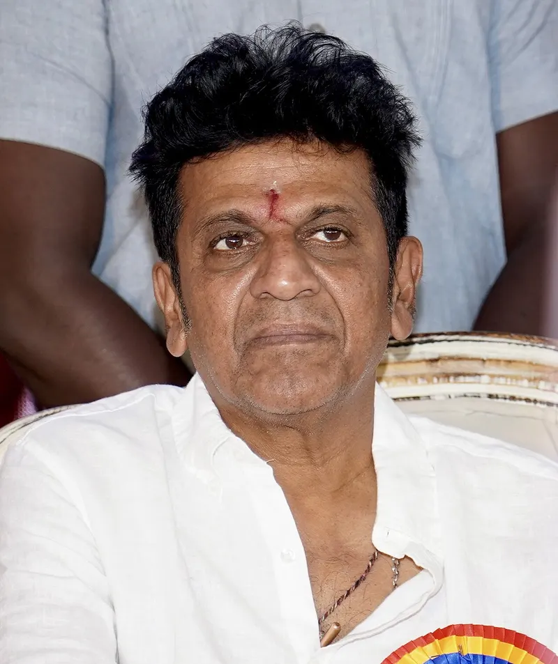 Shivarajkumar in a white shirt seated at a public event