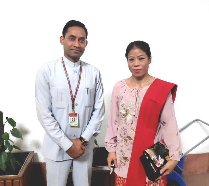 Mary Kom in a pink top and red stole standing beside a man