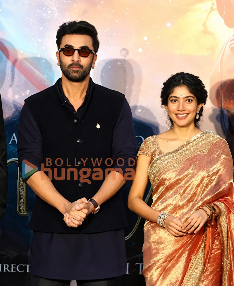 Ranbir Kapoor and Sai Pallavi standing together in front of a Ramayana poster