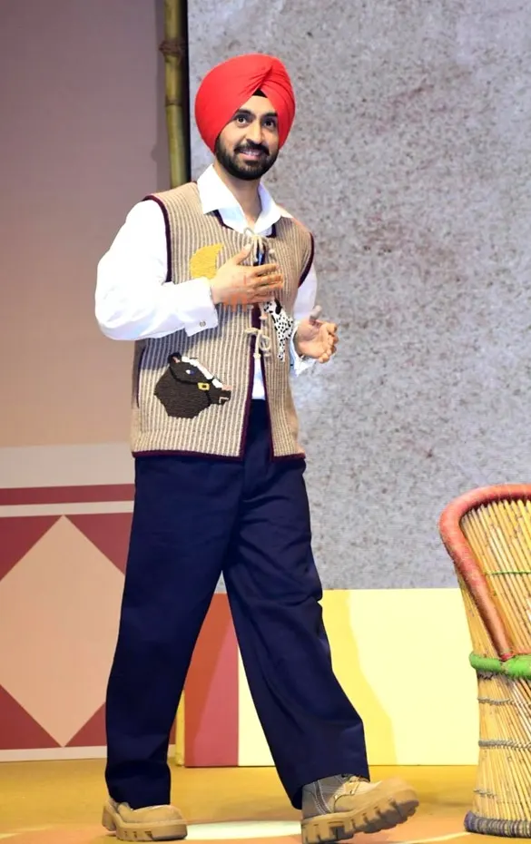 Diljit Dosanjh in a red turban and knitted vest walking on stage