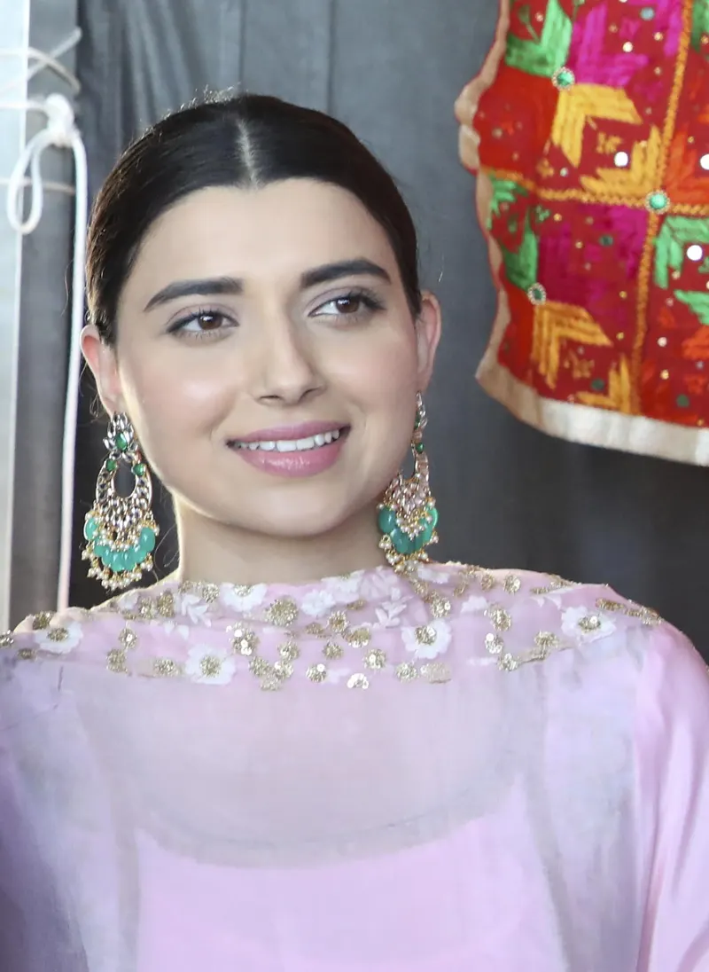 Nimrat Khaira smiling in a pink outfit and green earrings