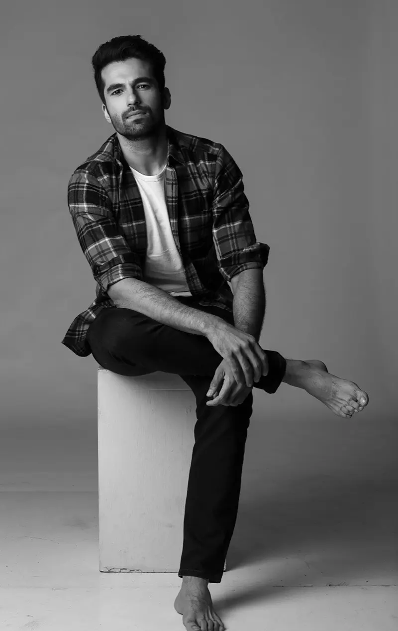 Ajay Sarkaria in a checked shirt seated on a white block, black and white portrait
