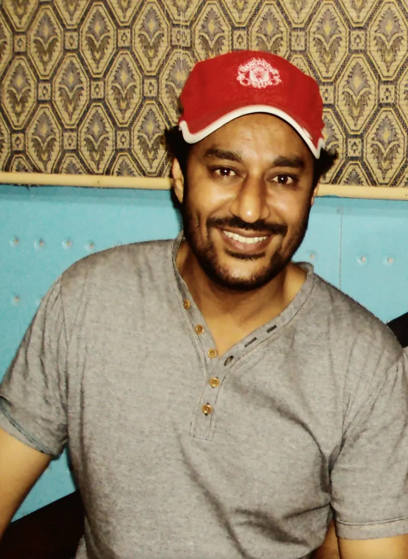 Harbhajan Mann smiling in a red cap and grey T-shirt