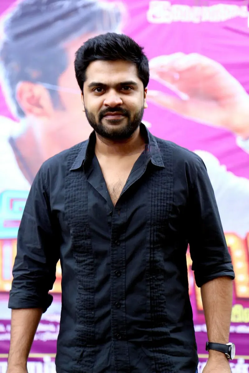 Silambarasan in a black shirt in front of a film poster