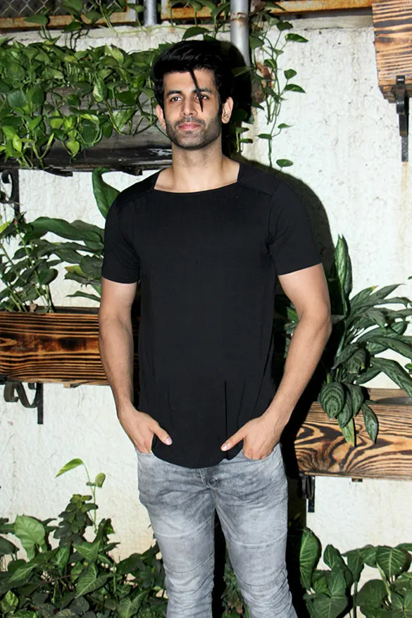 Namik Paul in a black T-shirt standing before a wall of plants