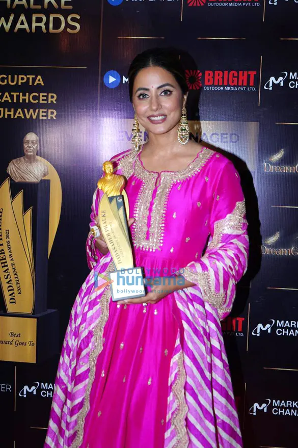 Hina Khan in a pink outfit holding an award trophy