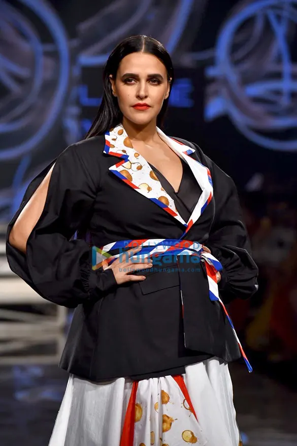 Neha Dhupia on a runway in a black jacket and printed skirt