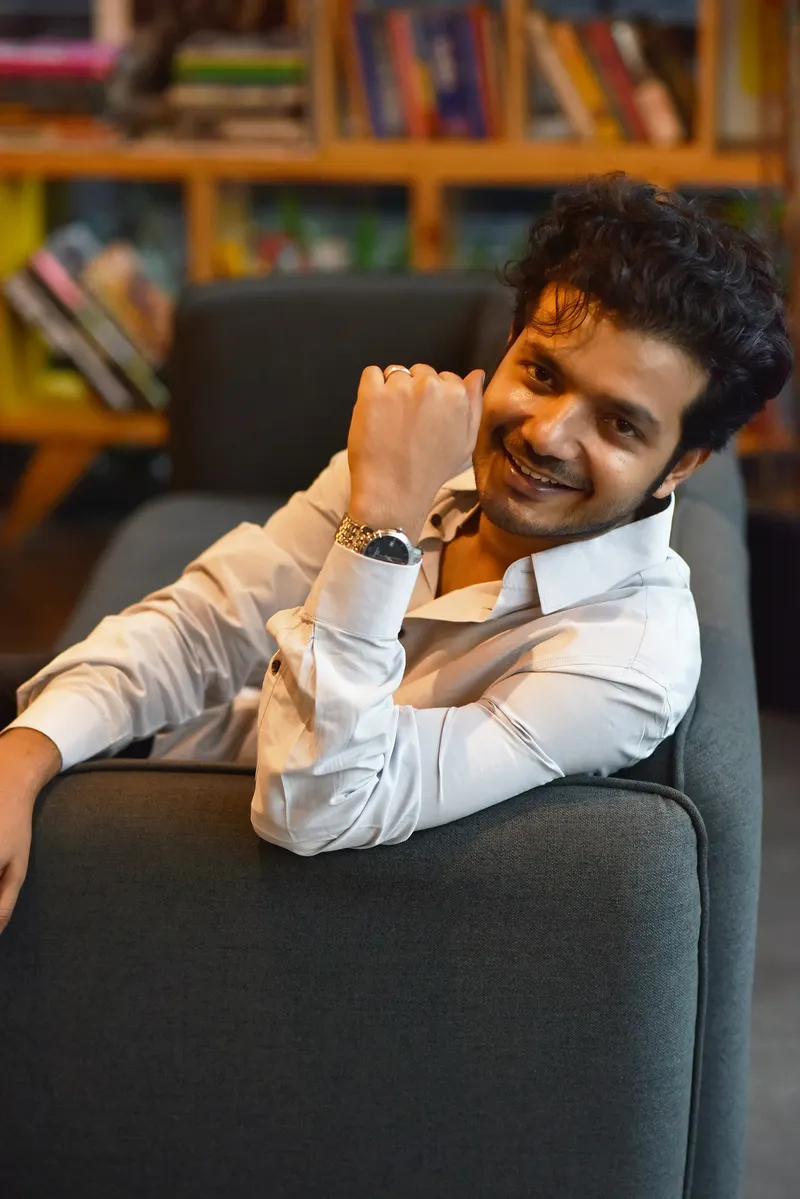 Sreenath Bhasi in a white shirt smiling on a sofa