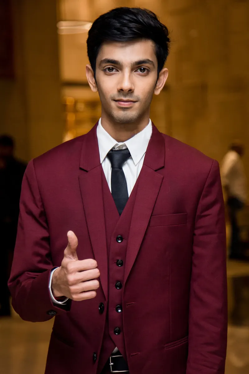 Anirudh Ravichander in a maroon suit giving a thumbs up